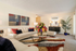 Inviting living room with modern decor, plush cream sofas, vibrant cushions, elegant glass coffee table, and colorful artwork for a stylish ambiance.