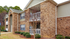 Charming two-story brick apartment building with cozy balconies and lush green surroundings.