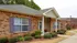Charming brick apartment with elegant columns, surrounded by manicured greenery and a welcoming pathway.