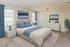 Elegant bedroom with plush carpet, featuring a luxurious bed with blue accents, modern white furniture, and natural light streaming through large windows.