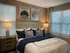 Cozy bedroom with elegant decor, featuring a plush bed adorned with blue accents, warm lighting, and modern art.