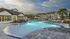 Inviting apartment complex with a sparkling swimming pool, modern clubhouse, and lush outdoor seating under a picturesque sky.
