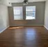 Bright apartment room with elegant wood flooring, natural light streaming through large windows, and a sleek ceiling fan.