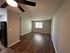Bright and spacious living area with modern ceiling fan and elegant wooden flooring, seamlessly connecting to a sleek kitchen featuring black appliances.