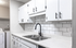Modern kitchen with sleek white cabinetry, subway tile backsplash, and stainless steel dual sink, adjacent to a convenient laundry nook.