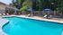 Inviting outdoor pool area with modern lounge chairs and vibrant blue umbrellas, surrounded by lush greenery, perfect for relaxation.