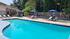 Inviting swimming pool area with sun loungers and umbrellas surrounded by lush greenery, perfect for relaxation.