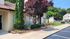 Charming apartment exterior with lush landscaping and a vibrant garden, featuring tall evergreens and colorful flowers.