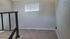 Bright and cozy room with plush carpet, natural light through a small window, and sleek black stair railing.