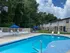 Charming apartment complex featuring a refreshing outdoor swimming pool, surrounded by lush greenery and stylish seating with blue umbrellas.