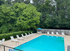Inviting outdoor pool area surrounded by lush greenery, featuring white lounge chairs and a charming umbrella table for relaxation.