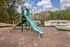Charming apartment complex with a vibrant playground featuring a slide, surrounded by lush trees and inviting outdoor space.