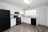 Modern kitchen with elegant white cabinets, sleek black appliances, and stylish wood flooring, bathed in natural light through large window.