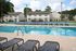 Inviting apartment complex featuring a sparkling swimming pool, multiple tennis courts, and charming two-story brick buildings surrounded by lush greenery.