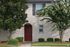 Charming townhouse exterior with welcoming red door, surrounded by lush greenery and brick facade.