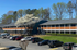 Charming two-story apartment building surrounded by lush greenery, featuring ample parking and beautiful spring blossoms.