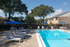Charming outdoor pool area with sun loungers and umbrellas, surrounded by lush trees and a picturesque brick apartment backdrop.