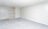 Spacious living room with plush gray carpet, modern shelving unit, and sleek white walls, perfect for stylish living.