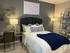 Cozy bedroom with elegant decor, featuring a comfortable bed adorned with plush cushions and a stylish blue throw, beside a modern glass desk and chic lighting.