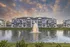 Elegant apartment complex with a scenic pond and fountain, framed by a stunning sunset sky.