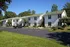 Charming white two-story apartment complex with green roofs surrounded by lush greenery and ample parking space.