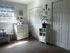 Bright and inviting bedroom featuring a chic white dresser, cozy seating, and lush green plants, perfect for relaxation.