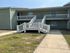 Charming two-story apartment building with a welcoming staircase and cozy balconies, surrounded by a lush green lawn.
