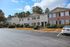 Charming apartment complex with two-story buildings, surrounded by lush greenery and ample parking spaces under a bright blue sky.