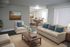 Elegant modern living room with plush beige seating, blue cushion accents, and a chic wooden coffee table, leading to a sophisticated dining area.