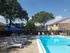 Inviting outdoor pool area with comfortable lounge chairs and blue umbrellas, surrounded by lush greenery and charming brick buildings.