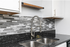 Modern kitchen design featuring sleek granite countertops, stylish subway tile backsplash, and a contemporary stainless steel faucet.