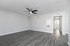 Spacious and contemporary living room featuring elegant gray flooring, modern ceiling fan, and a bright hallway leading to other rooms.