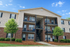 Charming two-story apartment building with spacious balconies, lush landscaping, and a pristine facade under a clear blue sky.
