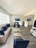 Bright and modern living room with sleek wooden flooring, plush blue and white furniture, and elegant decor.