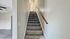 Sleek and modern hallway featuring a carpeted staircase with a wooden handrail, leading to a bright upper level in a stylish apartment.