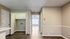Bright, inviting hallway with elegant wood flooring, leading to a sunlit room featuring a ceiling fan and large window.