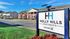 Charming Holly Hills Apartments nestled in a serene neighborhood, boasting brick exteriors and lush green surroundings under a clear blue sky.
