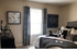 Elegant bedroom with luxurious bedding, stylish decor, and a chic wall clock near a sunlit window with patterned curtains.
