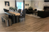 Elegant living and dining area with rustic wooden floors, featuring chic dark sofas, artistic dog-themed decor, and a large wooden table with decorative vases, enhancing the inviting ambiance.