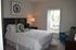 Inviting bedroom with a luxurious white bedspread, elegant decor, and ample natural light streaming through vertical blinds, creating a serene ambiance.