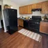 Charming kitchen with sleek black appliances, warm wooden cabinets, and a cozy rug on elegant wooden flooring.