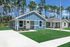 Charming blue and white cottage-style homes with manicured lawns set against a backdrop of tall pine trees under a bright blue sky.