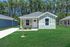 Charming single-story home with a welcoming front porch, nestled amid lush greenery and a serene wooded backdrop.