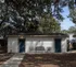 Charming outdoor area with a small white building, vibrant blue doors, and inviting seating under a canopy of lush trees.