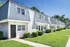 Charming townhouse complex with modern design, offering a series of white brick facades and lush landscaping under a bright blue sky.