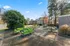 Vibrant outdoor space with modern green seating set on a spacious patio, surrounded by lush trees and well-maintained apartment buildings in the background.