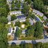 Aerial view of lush apartment complex surrounded by trees, featuring spacious units, ample parking, and inviting green spaces.