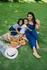 Joyful family picnic on a lush lawn, featuring a wicker basket with fresh juices and croissants, a colorful blanket, and a stylish sun hat.