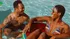 Joyful moment of two friends relaxing and laughing in a sunlit swimming pool, creating a vibrant summer vibe.