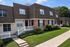 Inviting townhouses with charming architecture, featuring brick exteriors, classic white railings, and lush green lawns against a clear blue sky.